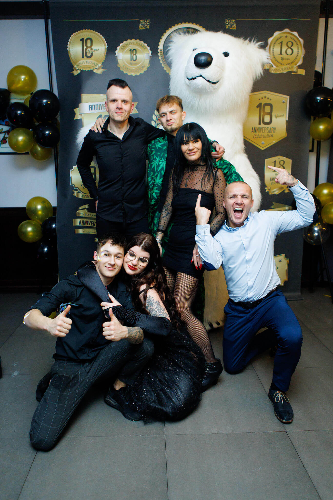 Group of people celebrating with a person in a polar bear costume at an anniversary event with golden balloons and awards-themed backdrop.