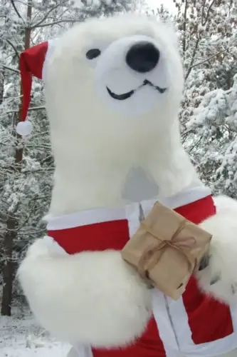 Giant polar bear dressed in a Santa suit, holding a wrapped gift, with snow-covered trees in the background.