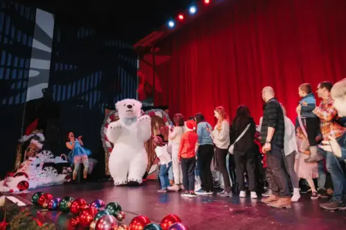 Children and adults on stage with a performer in a blue dress and a person in a polar bear costume at a Christmas event