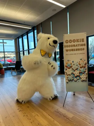 Person in polar bear costume next to a cookie decorating workshop sign in a modern office space.