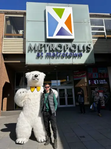 Man posing with a person in a polar bear costume in front of the Metropolis at Metrotown mall entrance.