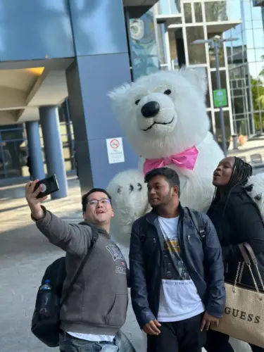 Three people taking a selfie with a person in a large polar bear costume outside a modern building.