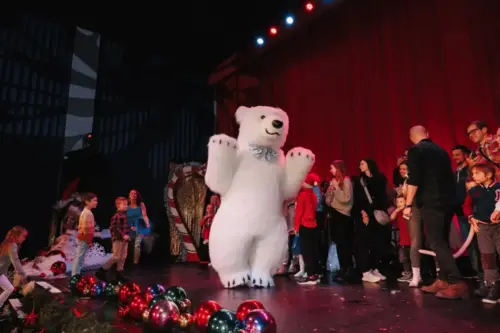 Animated children and adults on stage with a person in a polar bear costume during a Christmas celebration.
