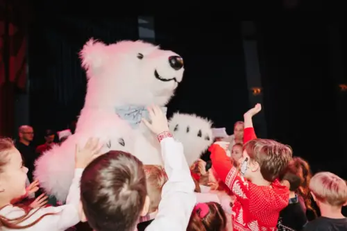 A person in a polar bear mascot costume surrounded by enthusiastic children reaching out to touch it during a festive event.