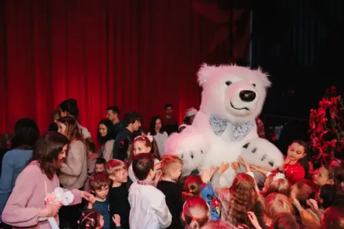 A group of excited children engaging with a person in a polar bear costume on a festively decorated stage.